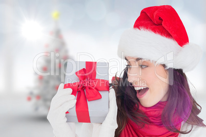 Composite image of astonished brunette in santa hat showing gift Composite image of astonished brunette in santa hat showing gift