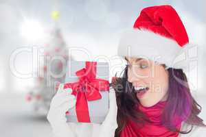 Composite image of astonished brunette in santa hat showing gift