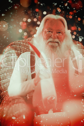 Composite image of happy santa writing list on the armchair