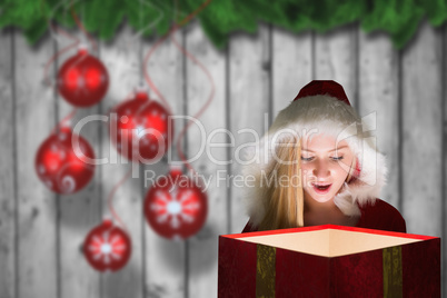 Composite image of festive blonde looking into glowing gift