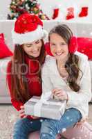 Composite image of festive mother and daughter opening a christmas gift