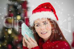 Composite image of festive redhead holding christmas gift