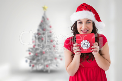 Composite image of festive brunette holding gift with bow