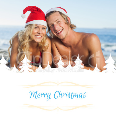 Composite image of couple lying on beach wearing christmas hats