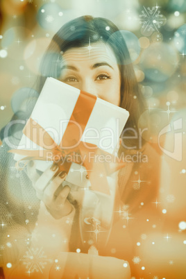 Composite image of brunette showing gift on the couch at christm