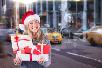 Composite image of festive blonde holding pile of gifts