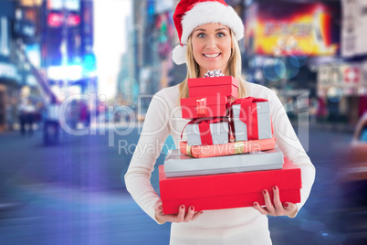 Composite image of festive blonde holding pile of gifts