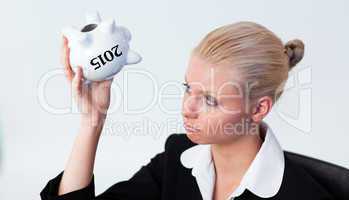 Composite image of sad business woman looking into piggy bank