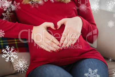 Composite image of close up of a pregnant woman doing heart sign