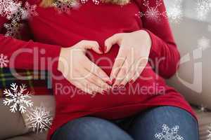 Composite image of close up of a pregnant woman doing heart sign