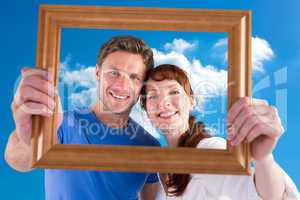 Composite image of couple holding frame ahead of them