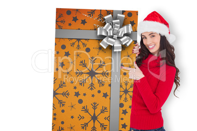 Composite image of smiling brunette in santa hat pointing gift c