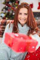 Composite image of festive redhead with gift on the couch