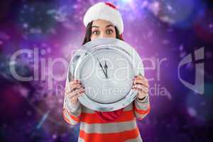 Composite image of festive brunette holding a clock