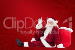 Composite image of santa sits leaned on his bag and waves