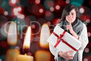 Composite image of brunette holding gift and keeping a secret