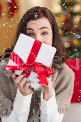 Composite image of brunette showing gift on the couch at christmas