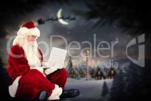 Composite image of santa sits and uses a laptop