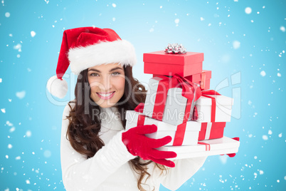 Composite image of festive brunette in santa hat holding pile of