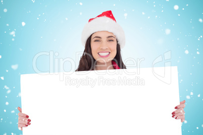 Composite image of smiling brunette in santa hat showing white p