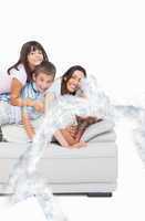 Composite image of children lying on their parents on sofa