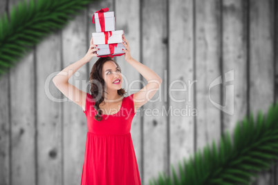 Composite image of happy brunette in red dress holding many gift