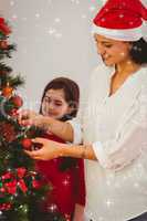Composite image of mother and daughter hanging christmas decorations on tree