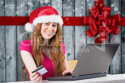 Composite image of festive redhead shopping online with laptop