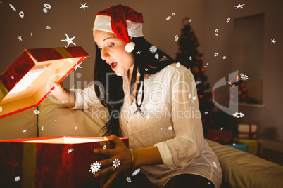 Composite image of festive brunette opening a glowing christmas