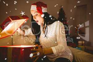 Composite image of festive brunette opening a glowing christmas