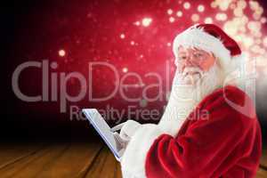 Composite image of santa uses a tablet pc and smiles into the ca