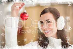 Composite image of pretty brunette with ear muffs holding bauble