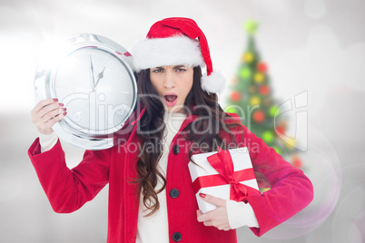 Composite image of surprised brunette holding a clock and gift