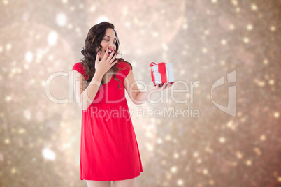 Composite image of astonished brunette holding a gift