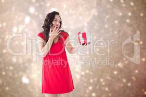 Composite image of astonished brunette holding a gift