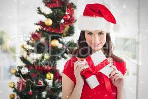 Composite image of festive brunette holding gift at christmas