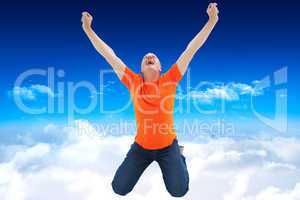 Composite image of mature man in orange tshirt cheering while kn