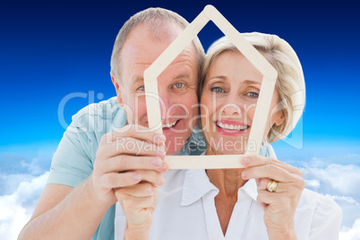 Composite image of happy older couple holding house shape