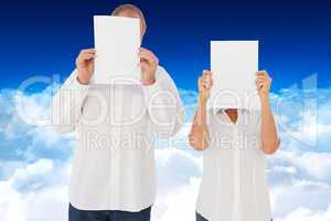 Composite image of couple holding paper over their faces