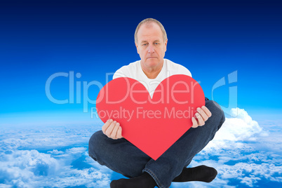 Composite image of upset man sitting holding heart shape