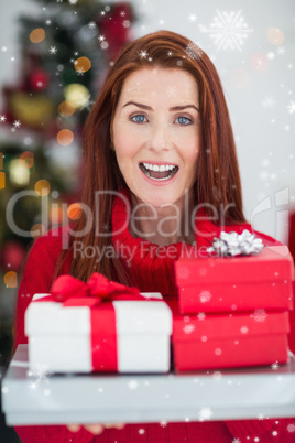 Composite image of festive redhead holding pile of gifts