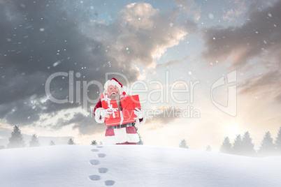 Composite image of santa carrying gifts in the snow