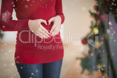 Composite image of close up of a pregnant woman making a heart o