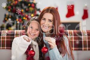 Composite image of festive mother and daughter holding baubles
