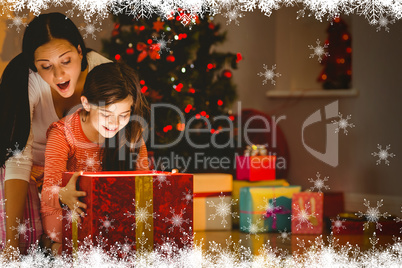 Composite image of festive mother and daughter opening a glowing