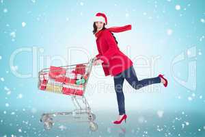 Composite image of festive brunette pushing trolley full of gift