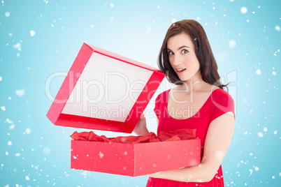 Composite image of surprised brunette in red dress opening gift