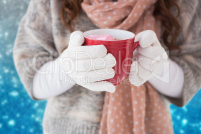 Composite image of woman in winter clothes holding a mug