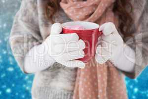 Composite image of woman in winter clothes holding a mug