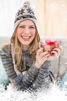 Composite image of happy blonde in winter hat sitting on couch showing a gift